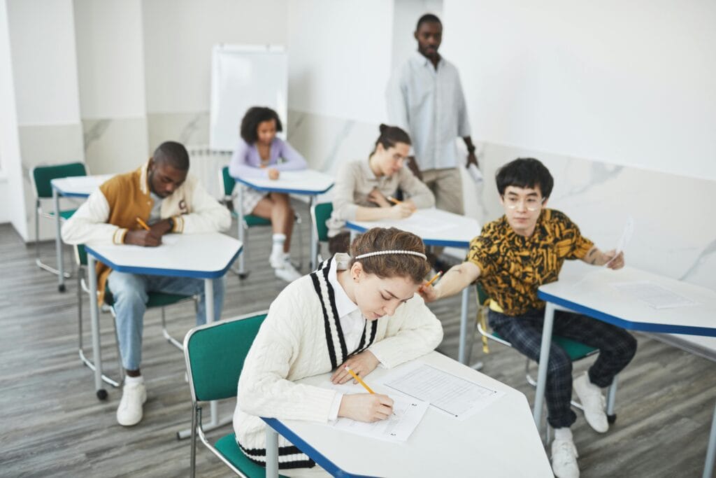 Group of students taking a test in a modern college classroom under teacher supervision.